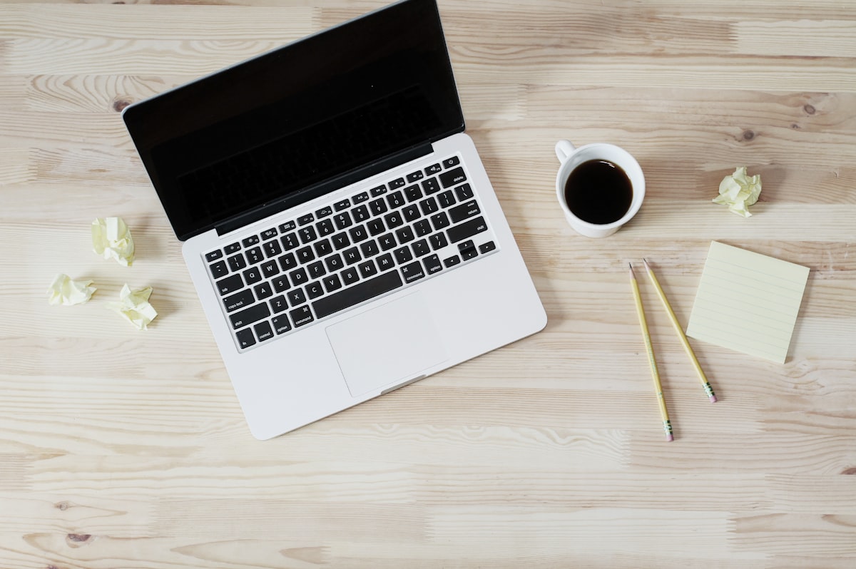 Ein Laptop mit Kaffee und Notizblock von oben auf hellem Holz